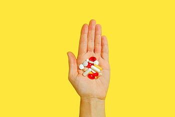 Close-up of an adult hand holding different types of pills against a vivid yellow background. HD wallpaper