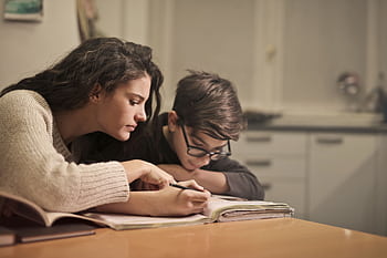An attentive girl helps her younger brother concentrate on homework in a cozy home setting. HD wallpaper