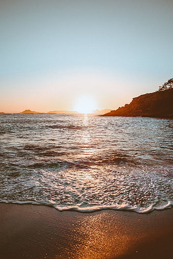 Tranquil sunrise over a beautiful beach with gentle waves and silhouetted coastline. HD phone wallpaper