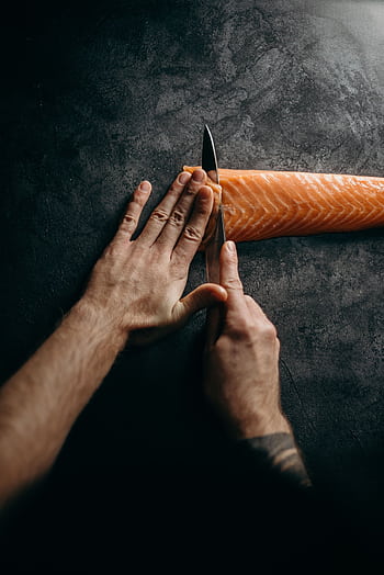 Chef expertly slicing fresh salmon on dark surface, highlighting culinary skill and precision in food preparation. HD phone wallpaper