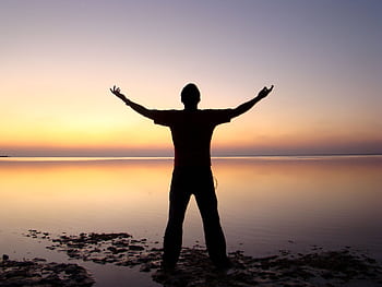 A person joyfully embracing the sunrise over a calm ocean, symbolizing dom and solitude. HD wallpaper