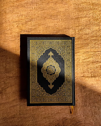 A beautifully decorated Quran resting on a rich brown wooden table, capturing spiritual essence. HD phone wallpaper