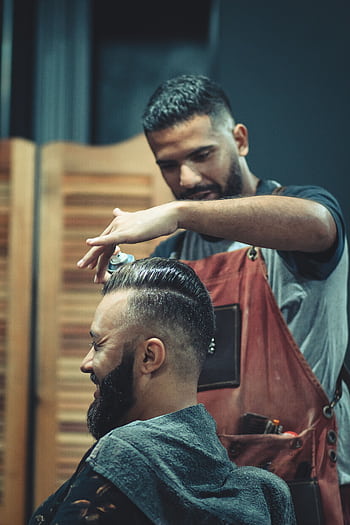 Skilled barber styling a man's hair in a modern barbershop setting, creating a trendy look. HD phone wallpaper