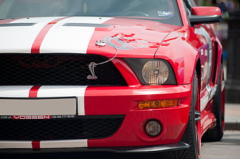 Front view of a red Ford Mustang sports car with white racing stripes in a city setting. HD wallpaper
