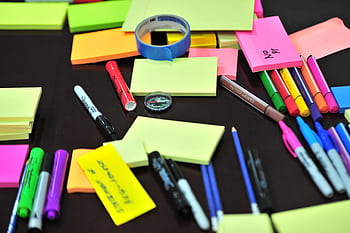 Colorful assortment of office supplies on a desk, including sticky notes, pens, and markers. HD wallpaper