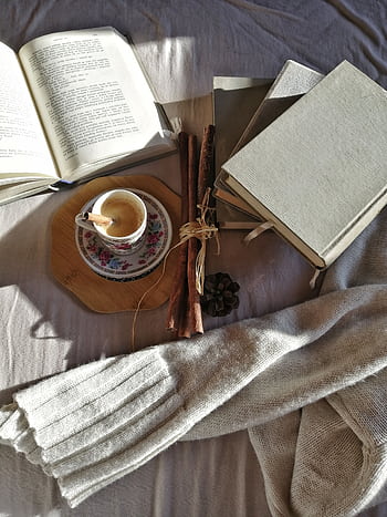 A warm setting featuring books, coffee, and a sweater in natural daylight creates a cozy reading atmosphere. HD phone wallpaper