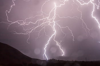 Captivating lightning bolts illuminate the night sky over dark hills in a dramatic weather display. HD wallpaper