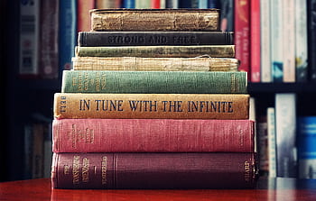 A stack of vintage hardcover books on a wooden table in a cozy library setting. HD wallpaper