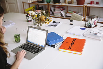 Woman works on a laptop in a stylish office, surrounded by books and documents. HD wallpaper
