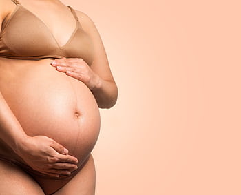 A pregnant woman gently cradles her belly, symbolizing motherhood and love. HD wallpaper