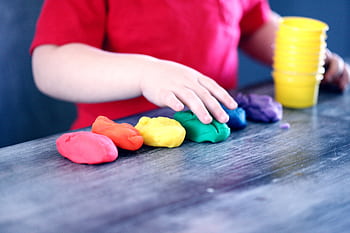 A young child with rainbow-colored modeling clay and stacking cups on a table indoors. HD wallpaper