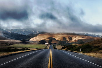 Dramatic sky over a deserted highway flanked by rolling hills, ideal for travel themes. HD wallpaper