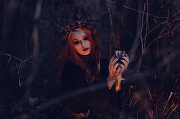 A mystical woman in gothic attire holds a chalice amidst a dark, eerie forest setting. HD wallpaper