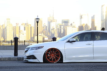 Custom lowered car with vibrant red rims against NYC skyline. Perfect for car enthusiasts. HD wallpaper