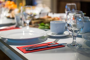 Close-up of an elegant dining table set with glassware, silverware, and red napkins in a restaurant setting. HD wallpaper