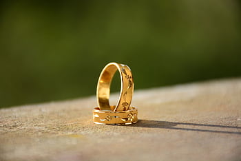 Close-up of two decorative gold wedding rings casting shadows on a warm surface. HD wallpaper