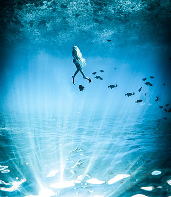 A captivating underwater scene featuring a lone diver illuminated by mystical blue light. HD phone wallpaper
