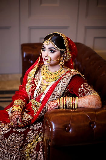 South Asian bride in traditional red and gold attire with henna and jewelry indoors. HD phone wallpaper