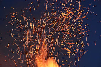 Vibrant orange sparks fly from a fire against a dark blue night sky, creating a dramatic visual. HD wallpaper