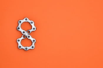Creative arrangement of bicycle chain links in the shape of the number eight on a bright orange background. HD wallpaper