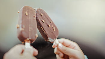 Close-up of two chocolate ice cream bars with nuts held by hands. HD wallpaper