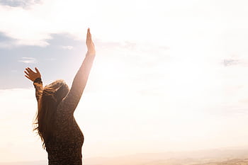 A woman with raised arms enjoying the bright open sky in a serene outdoor setting. HD wallpaper