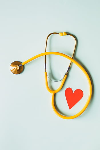 Yellow stethoscope arranged with a red heart cutout on a light green background, symbolizing heart health. HD phone wallpaper