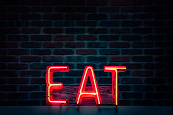 Vibrant neon 'EAT' sign in red glowing boldly against a dark brick wall background. HD wallpaper