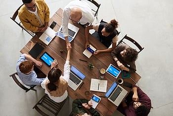 Top view of a diverse team collaborating in an office setting with laptops and tablets, promoting cooperation. HD wallpaper