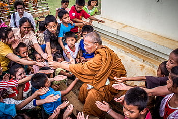 A Buddhist monk sharing gifts with children, capturing a moment of compassion and cultural tradition. HD wallpaper