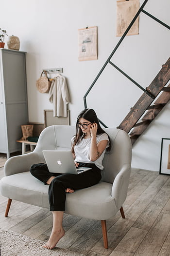 A woman sits comfortably on a sofa using a laptop in a modern living room. HD phone wallpaper