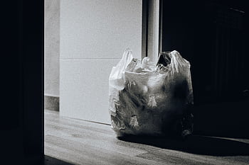 A dimly lit room containing a plastic bag filled with trash, emphasizing waste and recycling. HD wallpaper
