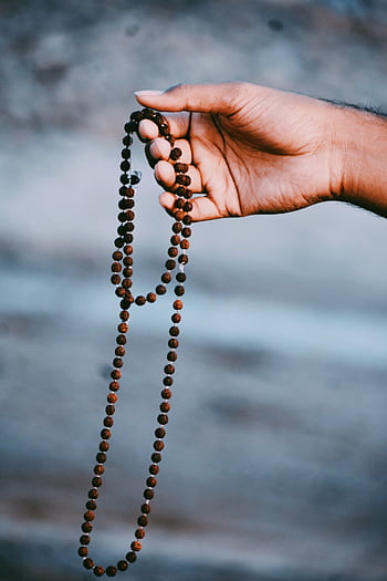 Close-up of a hand holding a Rudraksha bead necklace, symbolizing spirituality and meditation. HD phone wallpaper
