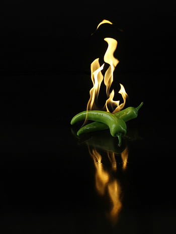 Dynamic of green chili peppers engulfed in flames over a dark reflective surface. HD phone wallpaper