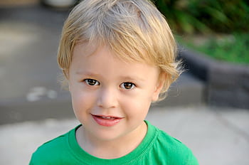 A cheerful blond child smiles outdoors in a green shirt, evoking innocence and joy. HD wallpaper