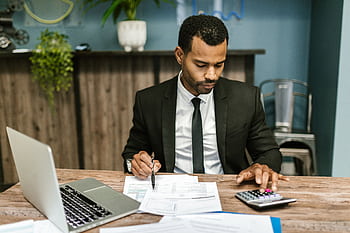A focused businessman works with a calculator and documents in a modern office. HD wallpaper