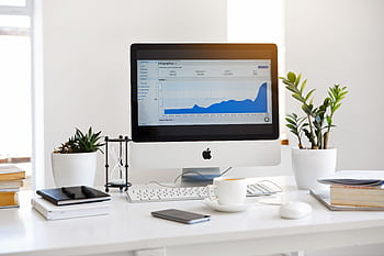 A clean, contemporary workspace featuring a with analytics on the screen and plants for a fresh look. HD wallpaper