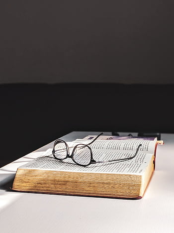 A pair of vintage eyeglasses lying on an open book on a minimalist table, perfect for reading themes. HD phone wallpaper