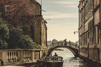 Captivating view of a Venetian canal with a bridge and boat, showcasing historic architecture. HD wallpaper