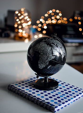Elegant black globe and notebook against warm bokeh lights, perfect for educational themes. HD phone wallpaper