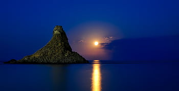 Peaceful sunset over the ocean with rock formation reflecting in calm waters. HD wallpaper
