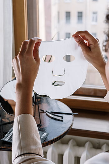 A woman holds a sheet mask in a cozy home setting, by a window. HD phone wallpaper