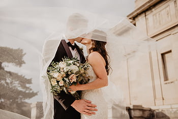 Bride and groom share a tender kiss under a veil, showcasing love and romance on their special day. HD wallpaper