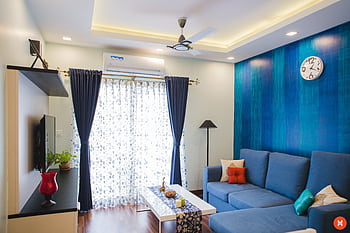 Modern living room with blue accents, featuring a sofa, wall clock, and natural light. HD wallpaper