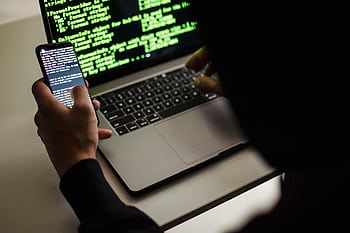A developer coding on a laptop and smart simultaneously in an indoor setting. HD wallpaper
