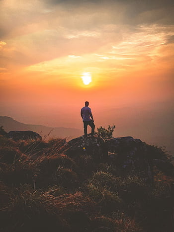 A lone hiker admires a stunning sunset view from Ponmudi Peak, creating a serene landscape scene. HD phone wallpaper