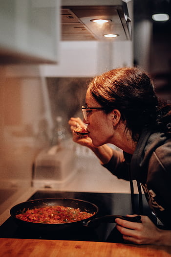 Woman cooking and tasting a dish on the stove, showcasing home culinary expertise. HD phone wallpaper