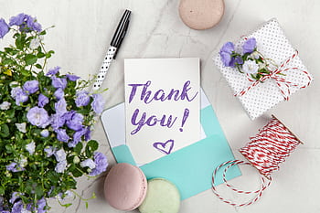 A beautifully arranged thank you card with lavender flowers, macarons, and gift package on a marble desk. HD wallpaper