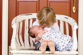 A tender moment captured between an older sibling and newborn, embracing love and family bonds. HD wallpaper