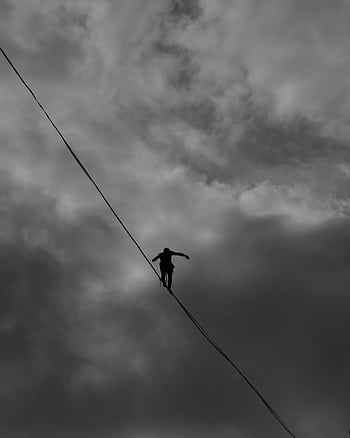 A silhouette of a person balancing on a tightrope against a dramatic, cloudy sky. HD phone wallpaper